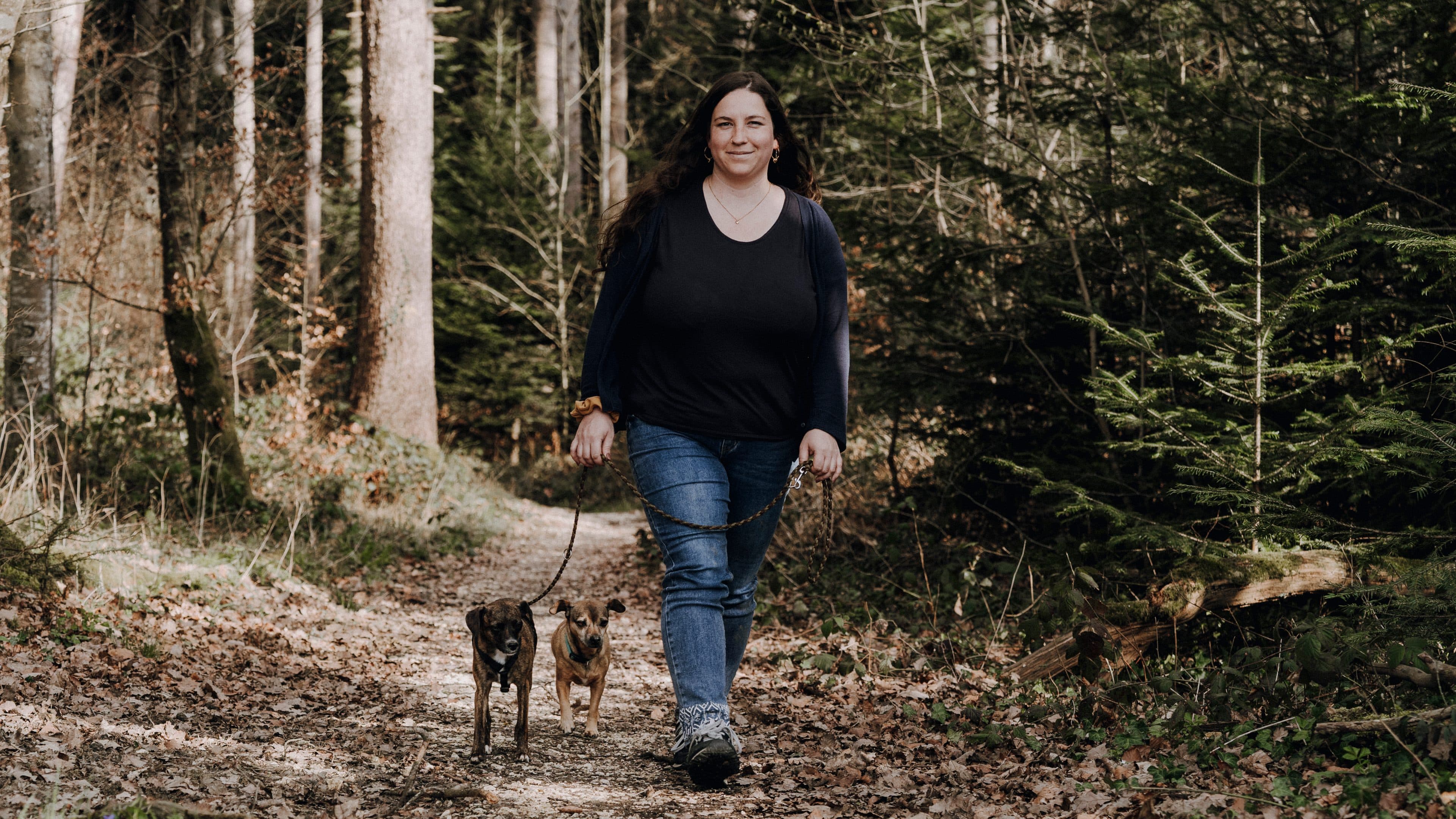 Liliane unterwegs auf einem Waldweg mit zwei Hunden an der Leine